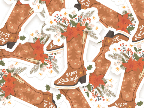 The Happy Yallidays Cowboy Boot Sticker by Onderkast Studio features a brown boot with festive greenery, poinsettia, berries, and “Happy Yallidays” in white. This durable water-resistant vinyl sticker is shown in an overlapping display.