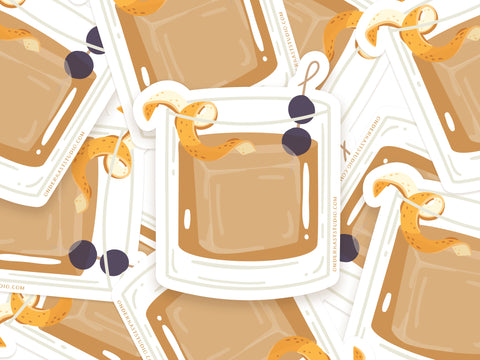 Onderkast Studio’s Old Fashioned Cocktail Sticker features a brown drink in a glass with an orange twist and cherries, styled for vintage flair and printed on weatherproof vinyl.