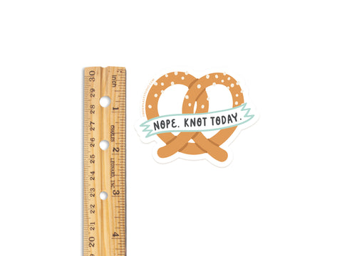 The Nope Knot Today Pretzel Sticker by Onderkast Studio is a water-resistant vinyl sticker featuring a salted pretzel and NOPE. KNOT TODAY. banner. Its about 2 wide, shown next to a wooden ruler for scale.