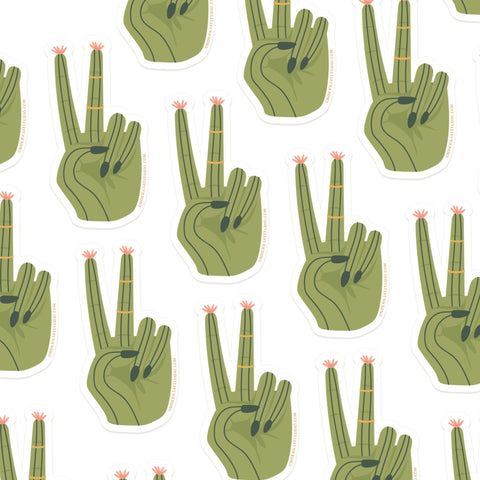 The Cactus Peace Sign Sticker by Onderkast Studio features a repeating green cactus hand making a peace sign with pink flowers on the fingertips, printed on durable vinyl against a crisp white background.