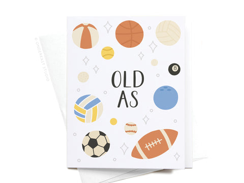 The Old As Balls Greeting Card by Onderkast Studio features playful OLD AS text with illustrated soccer, basketball, and footballs on a crisp white background—perfect for birthdays and offering a premium feel.