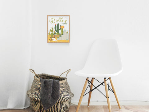 A modern, minimalist room with a white chair, woven basket, and Onderkast Studio’s Dallas Succulent Skyline Art Print framed on a white wall. The light wood floor adds warmth and highlights the chic desert vibe of the decor.