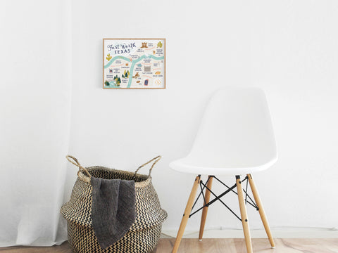 A modern, minimalist room features a white chair and woven basket on light wood floors. Above, the Fort Worth Map Art Print by Onderkast Studio in an illustrated style adds a premium feel to the white wall.