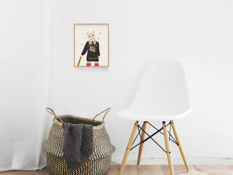A modern, minimal room with a white chair, a woven basket and blanket, and the Onderkast Studio TS Reputation Art Print featuring a cat in a sweater and red pants hanging on the white wall.