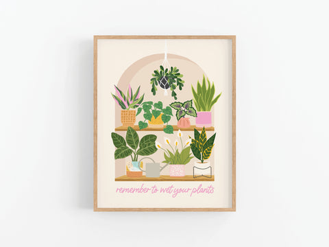 The Wet Your Plants Art Print by Onderkast Studio features a framed illustration of potted houseplants, shelves, a book, and watering cans with the phrase remember to wet your plants in pink for gardening humor.