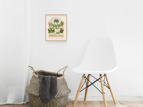 A white modern chair and a woven basket with a gray blanket sit against a white wall adorned with the playful Wet Your Plants Art Print by Onderkast Studio, adding botanical charm and gardening humor with its potted plant illustration.