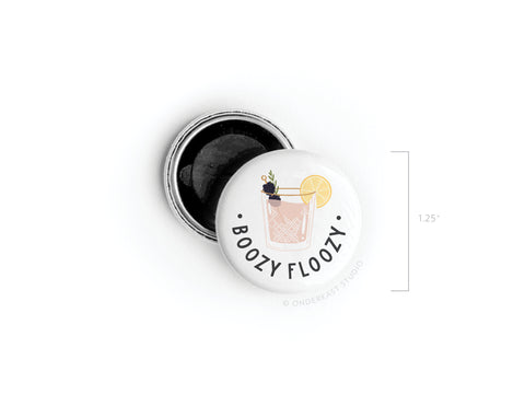 The Boozy Floozy Cocktail Button Magnet by Onderkast Studio is a 1.25 round, white magnet featuring a cocktail illustration with lemon and herbs, “BOOZY FLOOZY” text, and an open black backing for spirited style.
