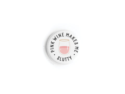 The Pink Wine Makes Me Slutty Button Magnet by Onderkast Studio features a round white design with a pink wine glass illustration and the phrase PINK WINE MAKES ME SLUTTY in black around it—perfect for wine lovers.