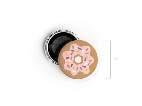 The Onderkast Studio Sprinkle Donut Button Magnet comes in a small, 1.25-inch round tin with a pink icing and sprinkles lid. The black interior is perfect for holding the magnet or other tiny treasures—a fun gift for donut lovers.