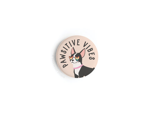 Bring some Pawsitive Vibe to your space with the Onderkast Studio Pawsitive Vibe Dog Button Magnet, featuring a smiling black and white dog in heart-shaped sunglasses and the words PAWSITIVE VIBES above.