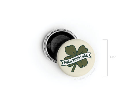 The Push Your Luck Clover Button Magnet by Onderkast Studio features a green four-leaf clover and Push Your Luck banner, measures 1.25 in diameter, and is shown next to its open black back.