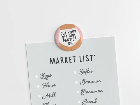 A grocery list held by the Put On Your Big Girl Panties Button Magnet from Onderkast Studio—featuring eggs, flour, milk, cheese, coffee, bananas, cinnamon, and bread—is a daily empowering women’s reminder.