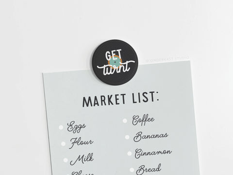 The Get Turnt Vinyl Button Magnet by Onderkast Studio holds a Market List with essentials like eggs, flour, and coffee—ideal for music lovers who appreciate high-quality everyday items.