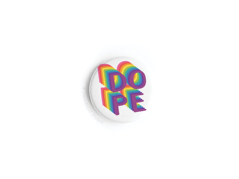 The Onderkast Studio DOPE Button Magnet is a stylish white circle with bold, 3D rainbow letters stacked in two rows on a plain background, crafted with high-quality production.