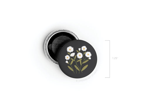 The Daisies Button Magnet by Onderkast Studio is a small, round black tin (1.25 wide) with a vibrantly colored lid featuring white daisies and green leaves—open to reveal the magnet inside, perfect as a charming floral accessory.