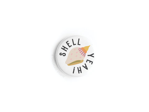 The Onderkast Studio Shell Yeah Button Magnet is a round white magnet with a pink conch shell illustration and SHELL YEAH! curved around it—perfect for ocean lovers and beach enthusiasts.