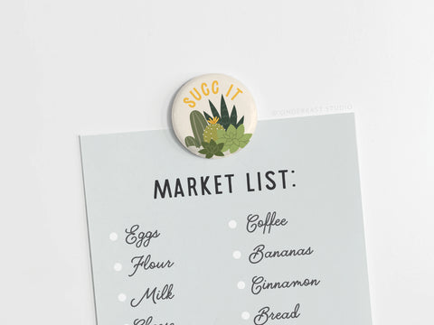 The Succ It Succulents Button Magnet by Onderkast Studio, featuring illustrated succulents and a witty phrase, is perfect for plant lovers to hold grocery lists or notes on any surface.
