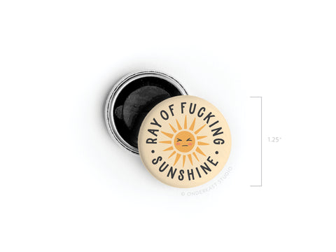 The Ray of Fucking Sunshine Button Magnet by Onderkast Studio features vivid colors and a cartoon sun with bold black text. It measures 1.25 in diameter and is shown beside its open metal back.