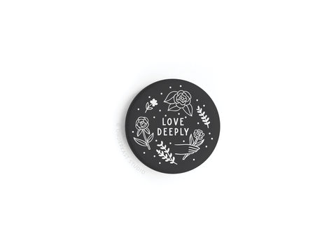 The onderkast studio Love Deeply Button Magnet (discontinued) is a 1.25 round black magnet with white line art of roses, stars, and dots, featuring LOVE DEEPLY in uppercase at the center.