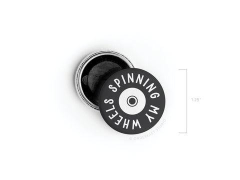 The Smagnetning My Wheels Button Magnet by Onderkast Studio is a discontinued 1.25-inch round black and white magnet featuring SPINNING MY WHEELS encircling a central circle, crafted with high-quality production.