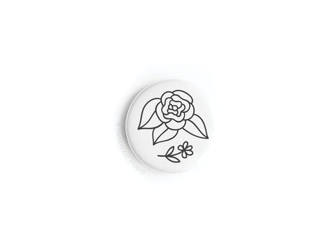 The Black Flowers Button Magnet by Onderkast Studio features a round white design with a minimalist black line rose, leaf, and small flower—perfect for lovers of simple floral décor.