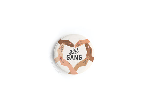 Celebrate female friendship with the Onderkast Studio Girl Gang Button Magnet, featuring four illustrated hands in different skin tones forming a heart around girl GANG on a white background in a stylish round design.