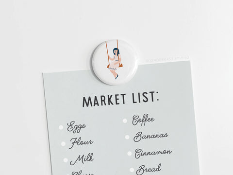 The Girl on a Swing Button Magnet by Onderkast Studio features a nostalgic illustration and securely holds your market list or notes on any magnetic surface.
