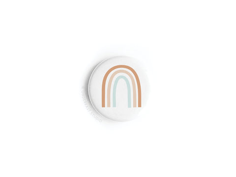 The Rainbow Button Magnet by Onderkast Studio features a minimalist design with three muted rainbow arches—tan, brown, and light blue—on a plain white background, offering a subtle yet vibrant symbol of inclusivity.