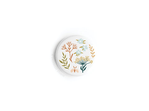 The Soft Florals Button Magnet by Onderkast Studio features a round white design with minimalistic florals and leaves in orange, yellow, blue, and green.