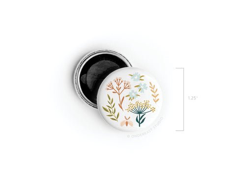 The Soft Florals Button Magnet by Onderkast Studio comes in a 1.25-inch round tin with a white lid decorated with wildflowers and leaves. The open tin reveals a black interior—ideal for storing the magnet or small keepsakes.