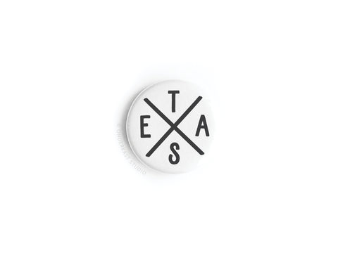 The Texas Logo Button Magnet by Onderkast Studio features a white round design with a black X dividing it into four sections, each displaying a black letter: E, T, A, and S, evoking a Texas-inspired logo on a clean white background.