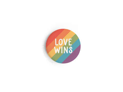 The Love Wins Button Magnet by onderkast studio features rainbow stripes and bold white LOVE WINS text—an eye-catching symbol of LGBTQ+ pride.