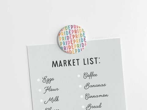 The Pride Button Magnet by Onderkast Studio, featuring the word PRIDE in rainbow colors, holds a grocery list (eggs, flour, milk, coffee, bananas, cinnamon, bread) against a light background.