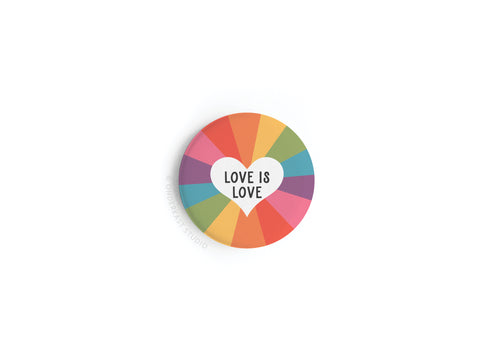 The onderkast studio Love Is Love Button Magnet features a round design with a rainbow background and a white heart at the center, showcasing vibrant colors that celebrate love’s universal message.