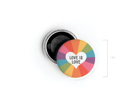 The onderkast studio Love Is Love Button Magnet is a 1.25 round magnet with a white heart and LOVE IS LOVE text, set against a vibrant rainbow background divided into segments. The pin is partially open, revealing the black interior.