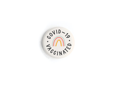 The Covid-19 Vaccinated Button Magnet by Onderkast Studio features COVID-19 VACCINATED encircling a colorful rainbow on white. Printed in the USA. Product is discontinued.
