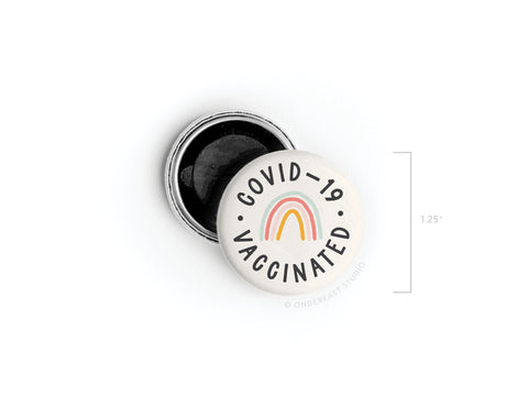 The Covid-19 Vaccinated Button Magnet by Onderkast Studio features a vibrant rainbow design and “COVID-19 VACCINATED” text on white, measures 1.25 inches, has a black interior, and is printed in the USA. DISCONTINUED.