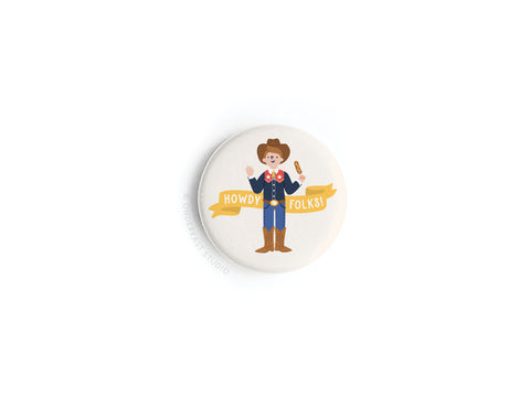The Howdy Folks! Button Magnet by Onderkast Studio features a cartoon cowboy with boots and hat holding a corndog, set against a white background with a yellow Howdy Folks! banner, inspired by Big Tex at the State Fair of Texas.