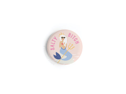 The Salty Bitch Mermaid Button Magnet by Onderkast Studio features an illustrated mermaid with long white hair, sunglasses, and a gold trident beneath SALTY BITCH in pink on a light pink background—ideal for beach lovers!.