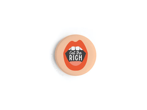 The Eat the Rich Button Magnet by Onderkast Studio features red lips biting bold Eat the Rich text, set against a light peach background for a playful, eye-catching statement on economic justice.
