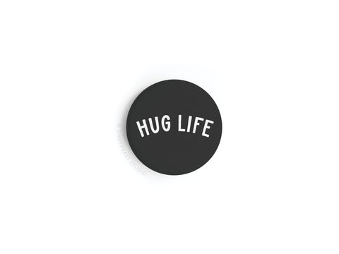 The Hug Life Button Magnet by Onderkast Studio features bold white HUG LIFE text on a black circular background—a stylish, cozy accent for any space.
