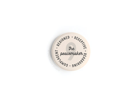 The Enneagram Button Magnet – 9 The Peacemaker by Onderkast Studio is a round beige magnet with the number 9 at the center, featuring words like compliant, complacent, resigned, receptive, and reassuring around the edge.