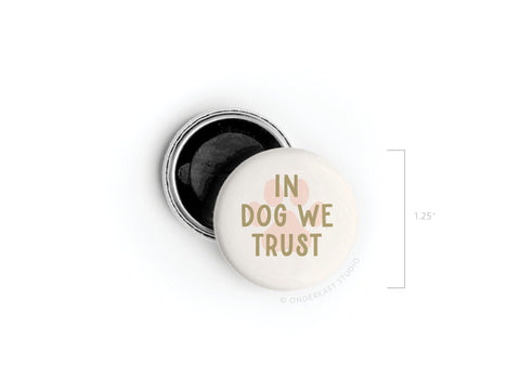 The In Dog We Trust Button Magnet by Onderkast Studio features bold text on a light 1.25 round design, perfect for dog lovers. The reverse side reveals its metal back and pin mechanism.