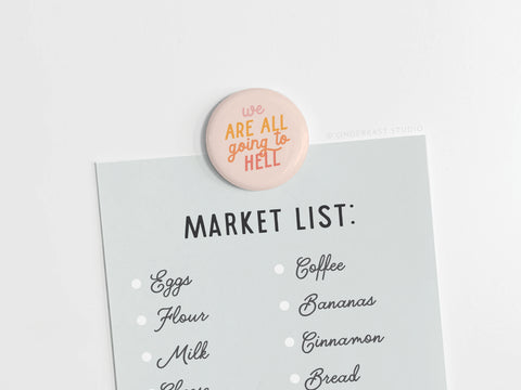 A grocery list—eggs, flour, milk, coffee, bananas, cinnamon, and bread—is held up by the vibrant “We Are All Going to Hell Button Magnet” from Onderkast Studio.