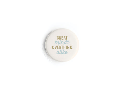 The Onderkast Studio “Great Minds Overthink Alike” Button Magnet features gold and light blue text on a round white background—a witty gift for fans of clever sayings.
