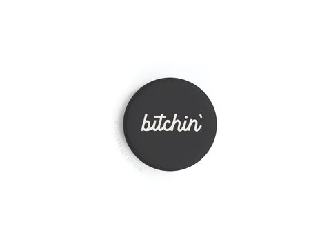 The Bitchin’ Button Magnet by Onderkast Studio features retro style: a black round pin with “bitchin’” in crisp white cursive, centered on a plain white background.