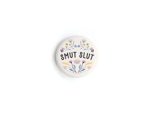 The Smut Slut Button Magnet by Onderkast Studio features bold black SMUT SLUT text with floral art on a white background—a fun literary accessory for fans of spicy reads and bookish humor.