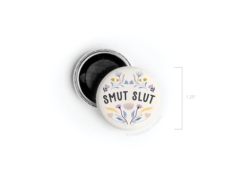 The Smut Slut Button Magnet by Onderkast Studio features pastel floral designs and bold SMUT SLUT text on a 1.25-inch white pinback—ideal for fans of spicy reads.