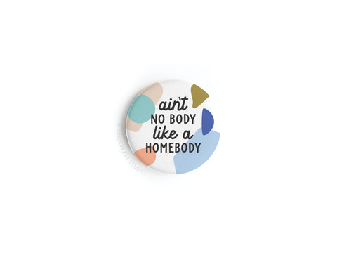 The Ain’t No Body Like a Homebody Button Magnet by Onderkast Studio features abstract pastel shapes and uplifting text—perfect for introverts. Displayed on a round, white background.