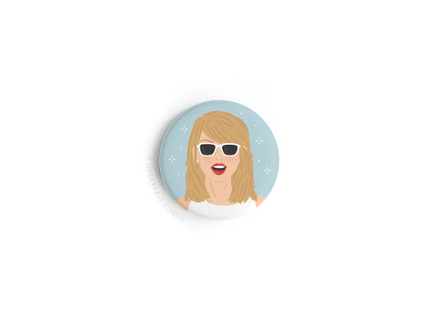 The TS 1989 Button Magnet by Onderkast Studio features a blonde woman with white sunglasses and red lipstick on a light blue background with white stars—pop perfection inspired by Taylors hit album.